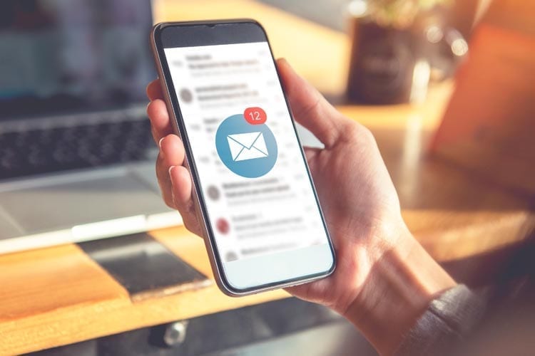 woman checking her email on phone and laptop Boston Luxury Homes Real Estate